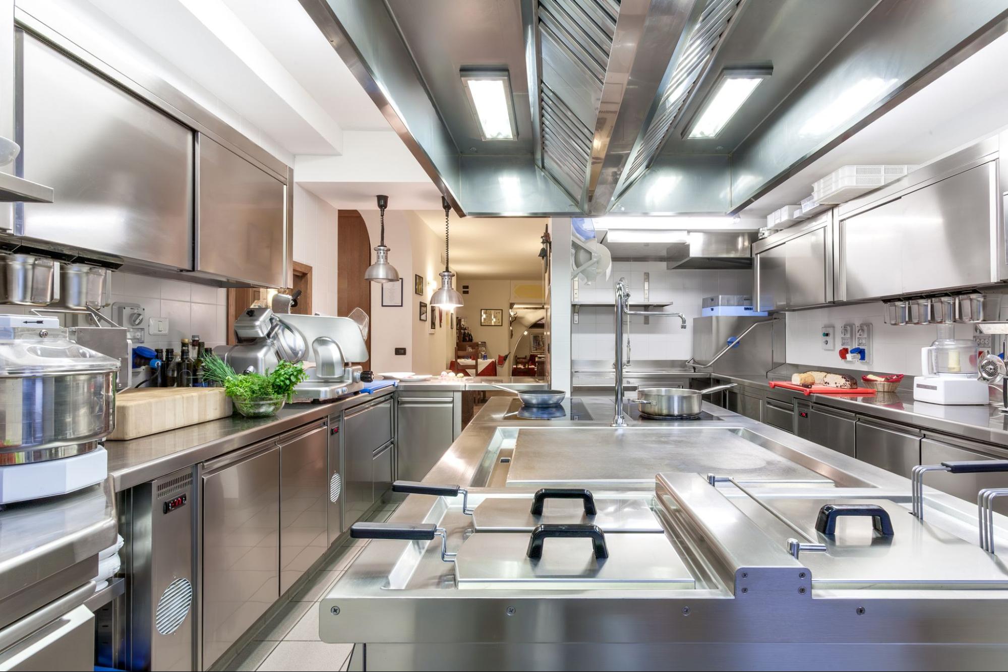 Commercial kitchen with stainless steel cooking equipment, preparation counters, ventilation hoods, and clean food service work areas.